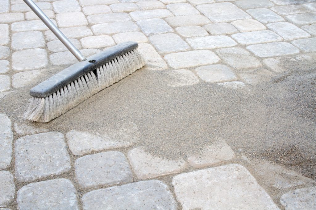 Broom sweeping sand between pavers.