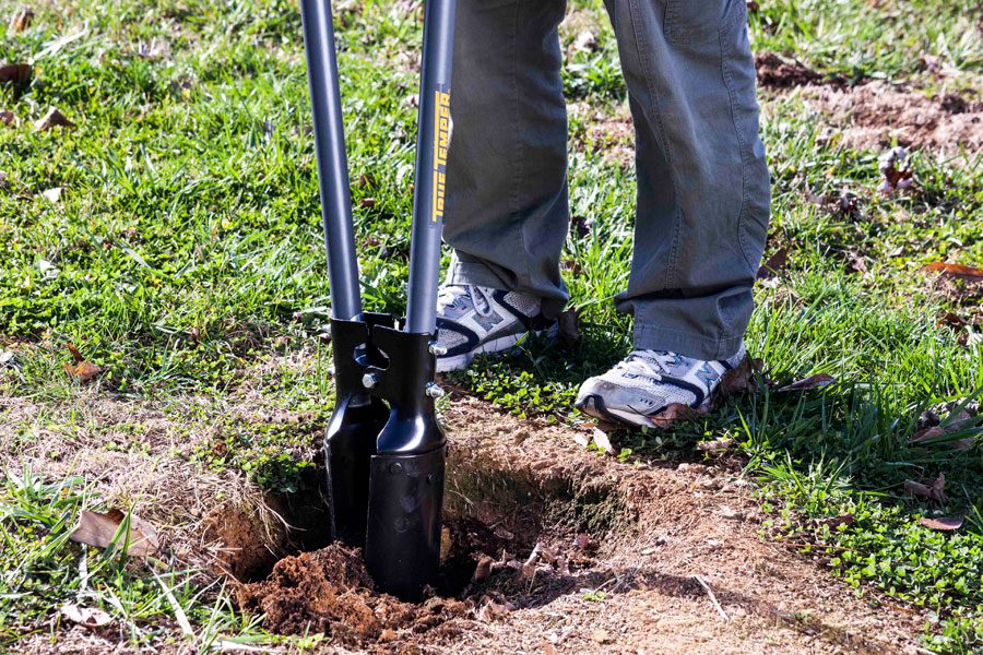 Person using a post hole digger to open a hole in the ground.