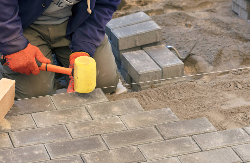 Worker wearing a rubber hammer to set concrete pavers on a construction site.