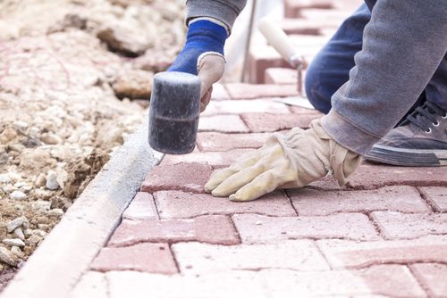 Close up of a person installing pavers with a rubber hammer.