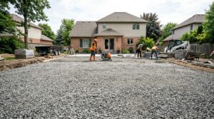Wide shot of a backyard construction site showing what is paver base used for as a foundation for a new stone patio.