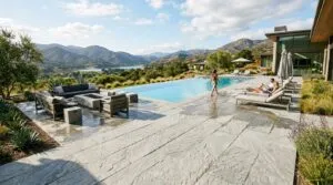Wide view of a luxury patio and pool area featuring light colored cool touch pavers under bright natural sunlight.